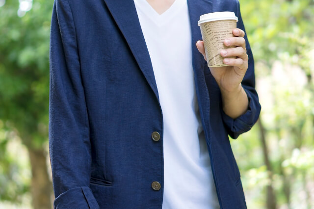 コーヒーを持つジャケットの男性